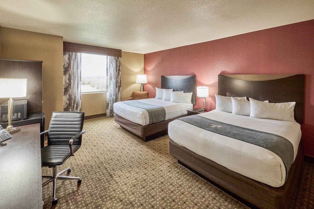 A hotel room with two beds, a desk with a chair, a TV, and a window with curtains.