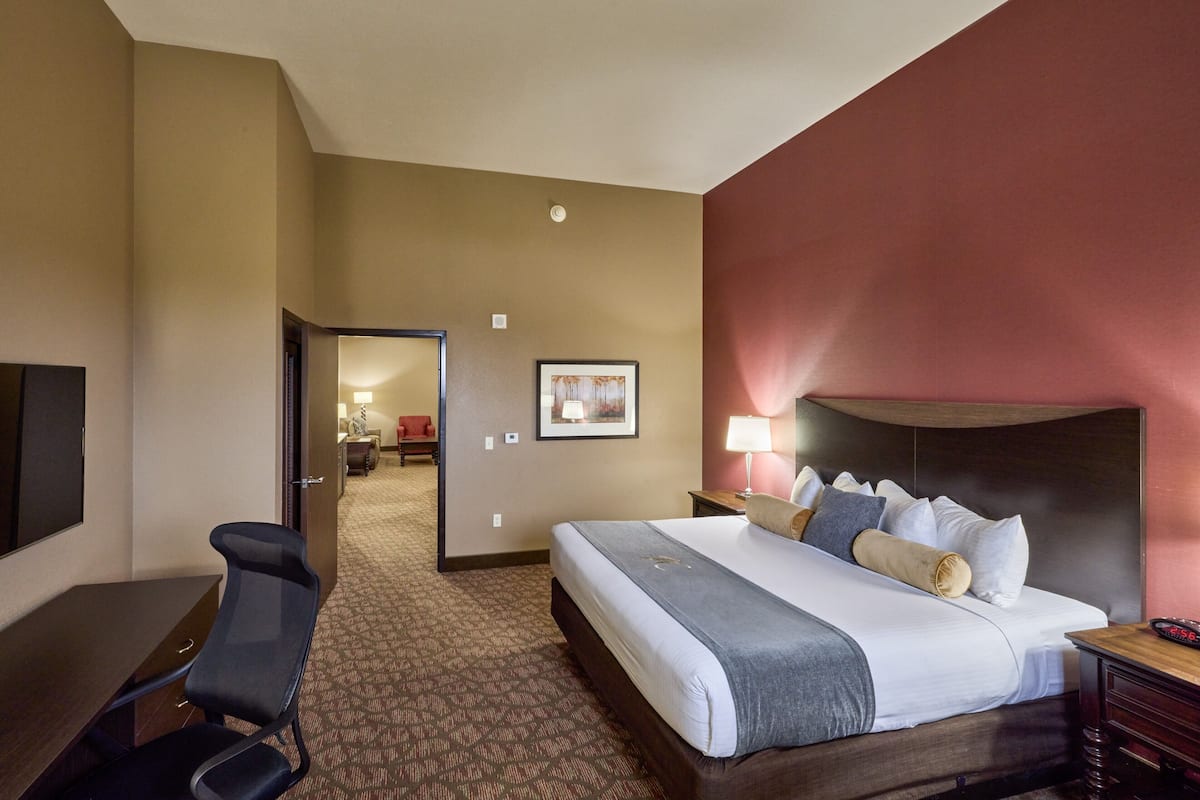 A hotel room with a bed, desk, chair, and a hallway leading to another room.