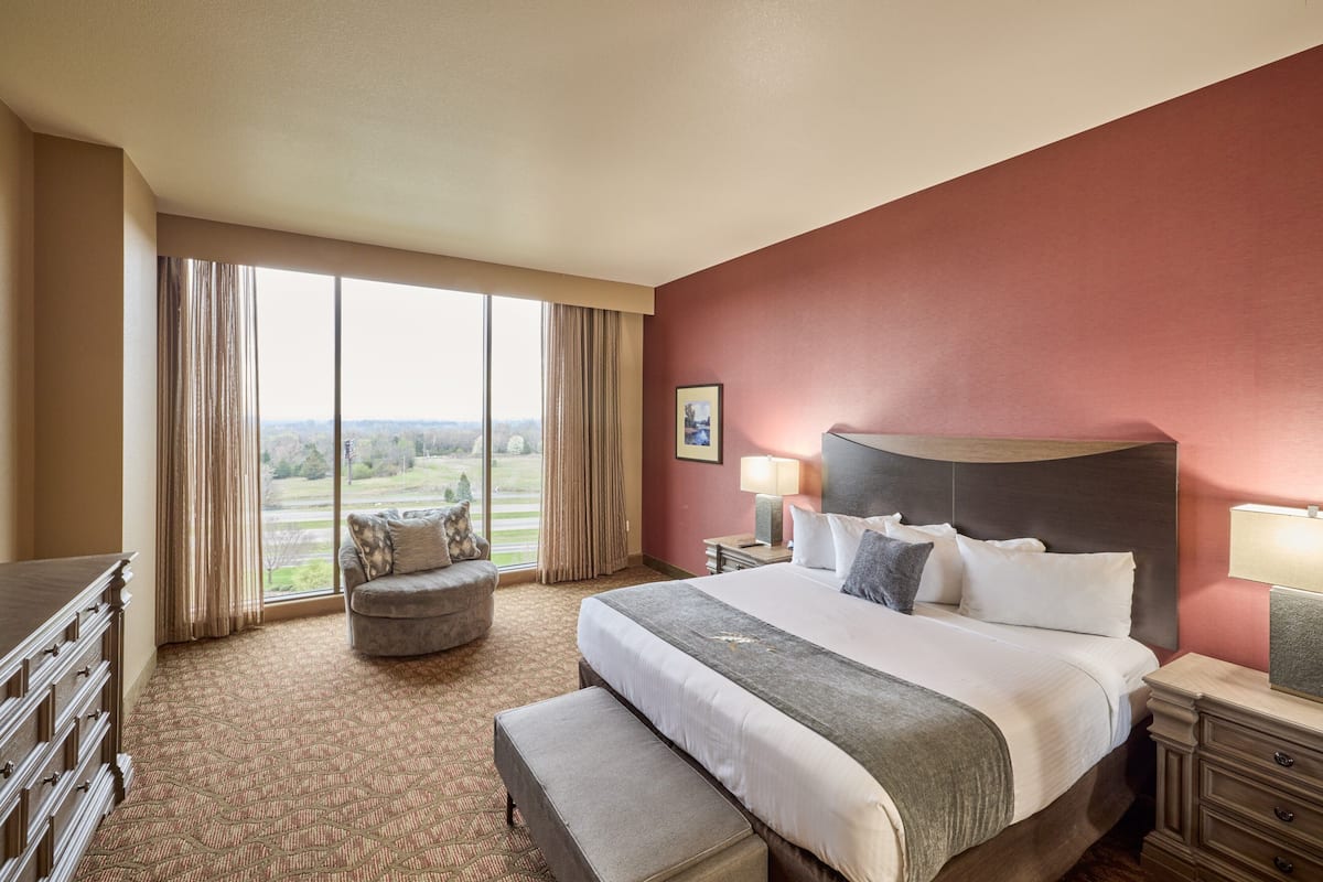 A hotel room with a large bed, a desk, a chair, and a view of the outdoors.