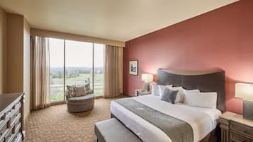 A hotel room with a large bed, a desk, a chair, and a view of the outdoors.