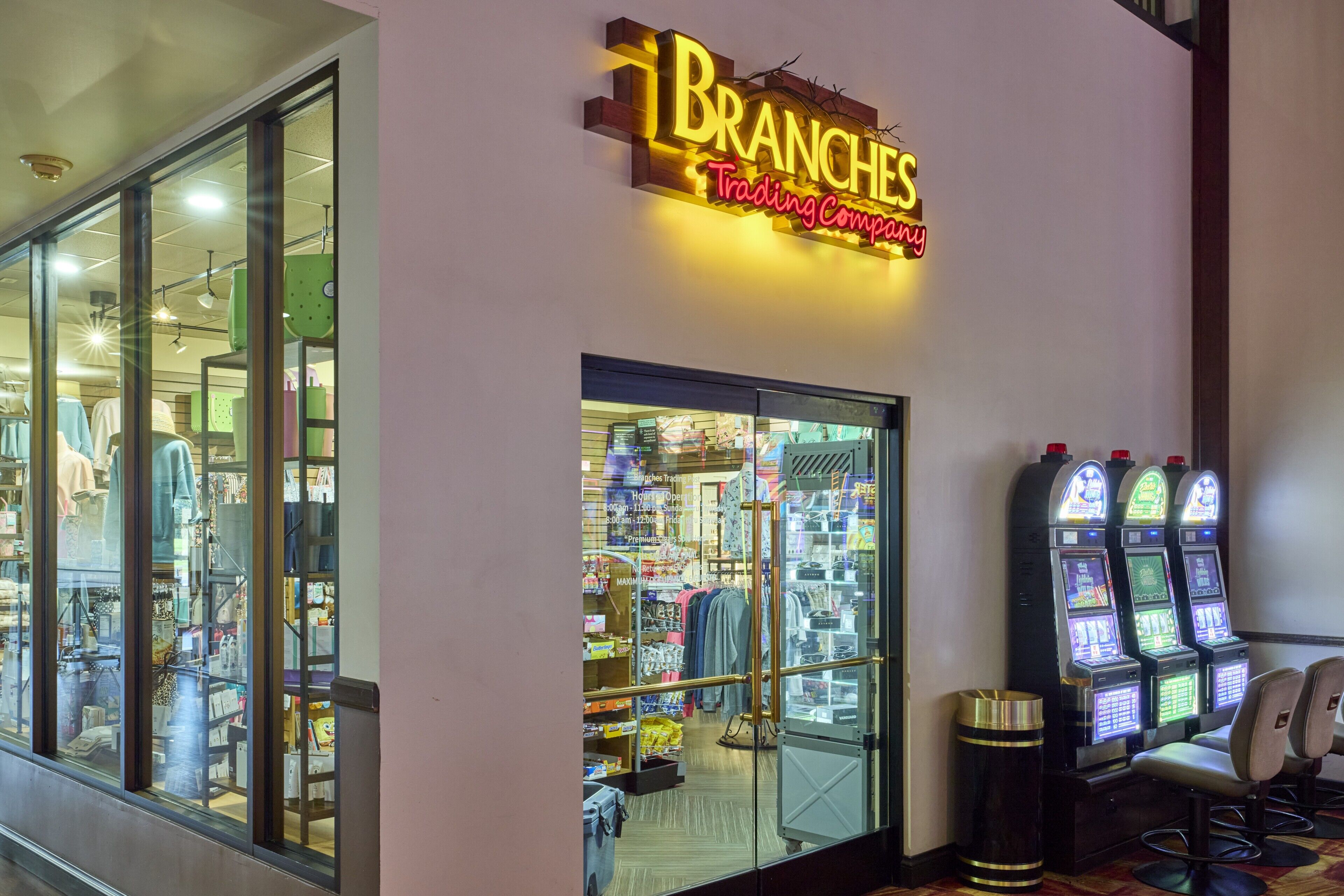 A storefront with a neon sign reading 'Branches Trading Company,' glass doors, and slot machines.