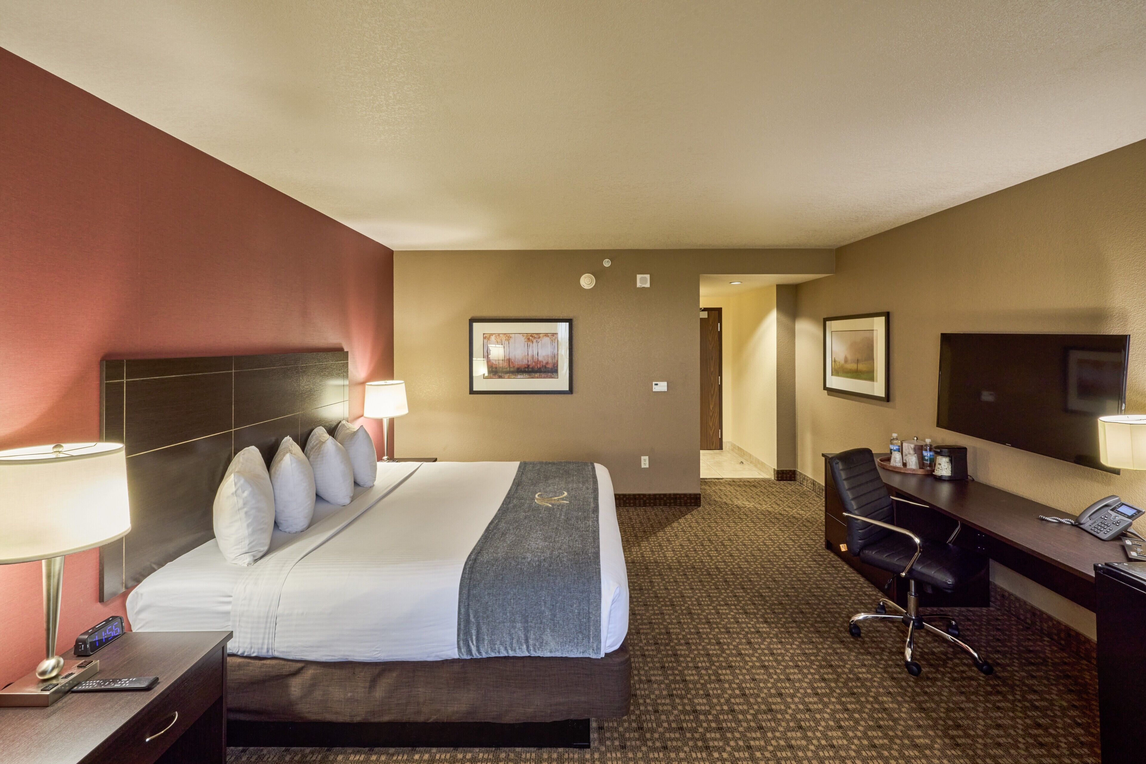 Quarto de hotel com cama, escrivaninha, cadeira, luminária e telefone.