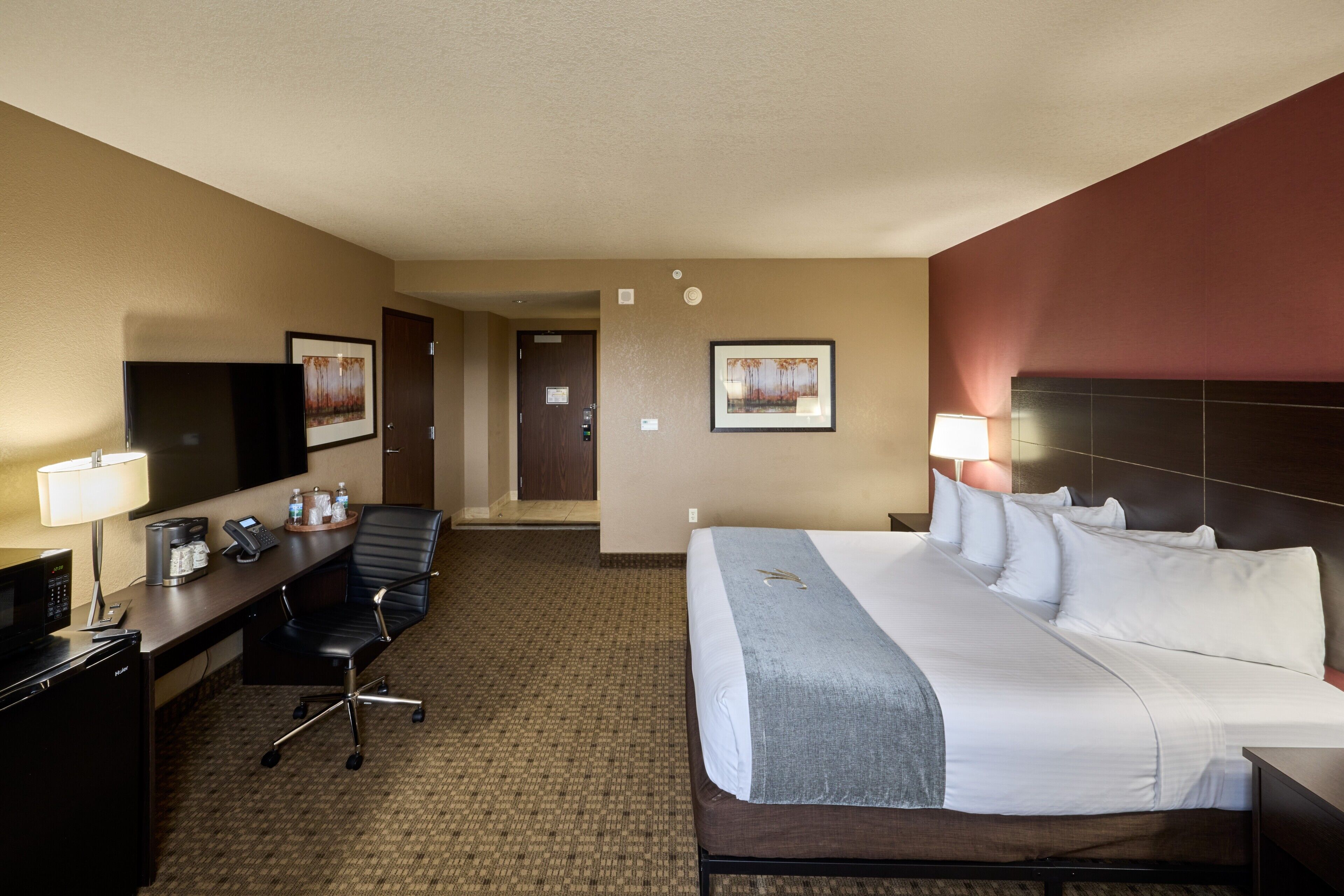 A hotel room with a bed, desk, chair, television, and a door leading to another room.