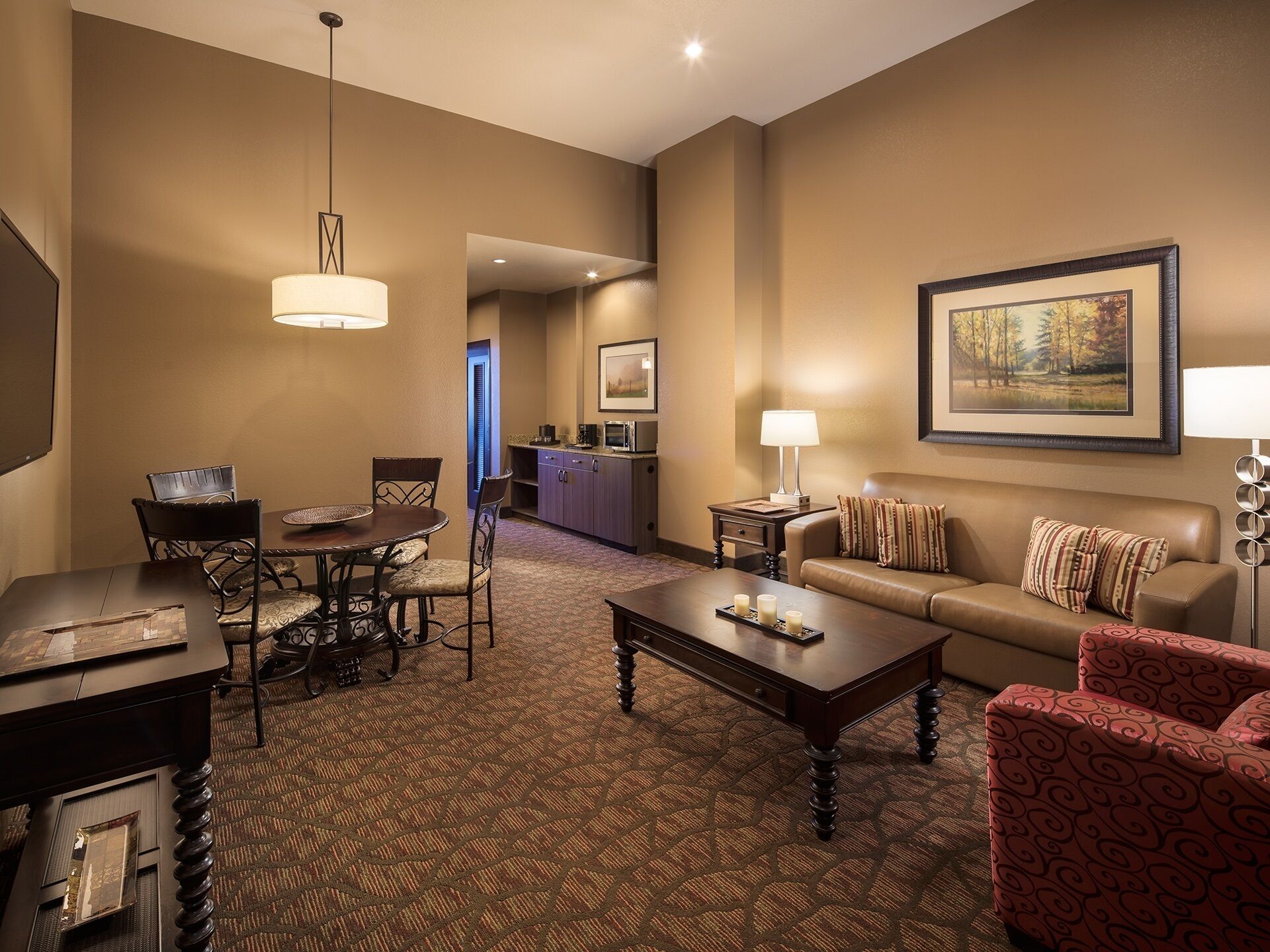 Habitación de hotel con comedor, sofá, mesa de centro y un cuadro en la pared.