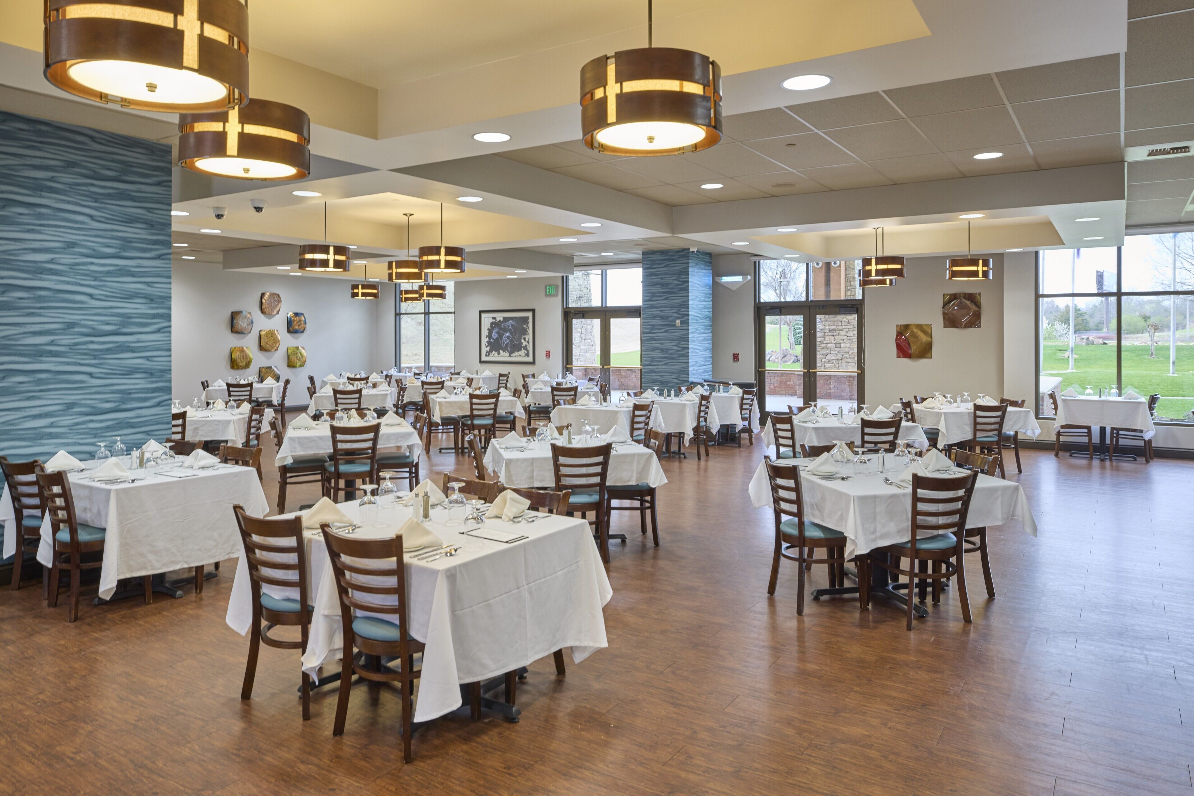 A spacious dining area with multiple tables and chairs, large windows, and hanging pendant lights.