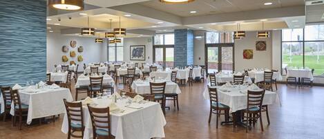 A spacious dining area with multiple tables and chairs, large windows, and hanging pendant lights.