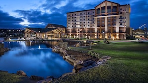 A hotel with a large building, a pond, and a well-maintained lawn. - Choctaw Casino & Resort Pocola, Trademark Coll by Wyndham (Pocola)