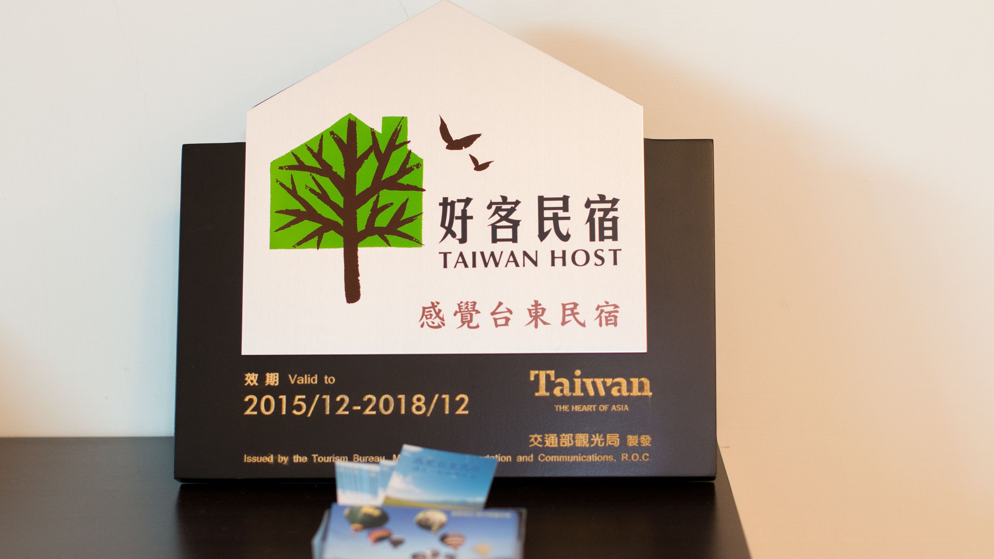 Letrero del hotel Taiwan Host con un logotipo de árbol, texto bilingüe y una fecha de validez.