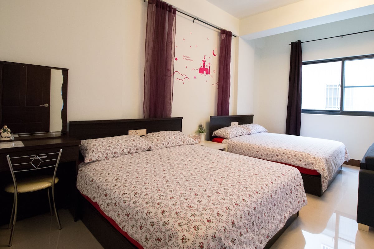 A hotel room with two beds, a desk, a chair, and a window with curtains.