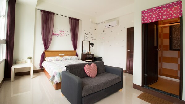 A bedroom with a bed, a bedside table, a grey sofa with a heart-shaped pillow, a desk with a chair, and a wardrobe with a pink heart-patterned curtain. - Fu Taitung B&B (Taitung)