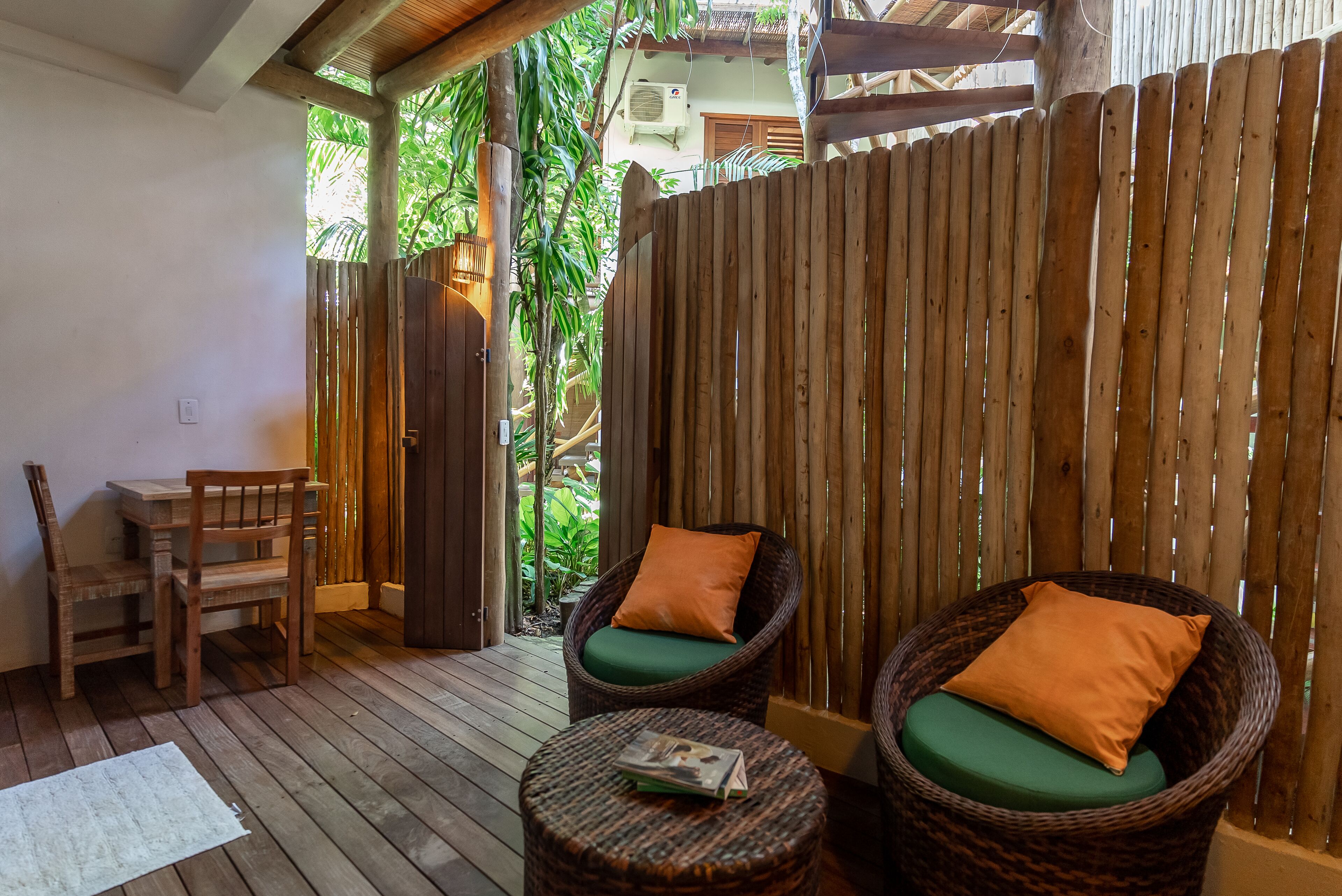 A wooden deck with wicker chairs and a table, surrounded by a bamboo fence.