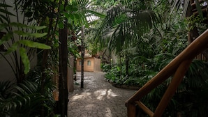 A cobblestone pathway leading through a lush indoor garden with various plants and a wooden structure in the background.