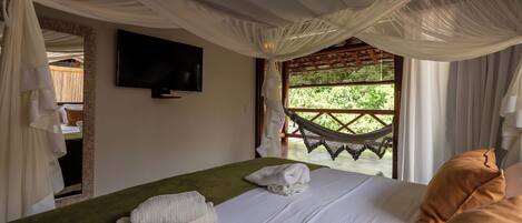 Quarto com cama, televisão, rede do lado de fora da janela e vista para o verde.
