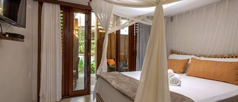 Ein Schlafzimmer mit Bett, Vorhängen, Fernseher und Blick ins Freie.