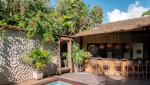 A poolside area with a bar, wicker chairs, and potted plants.