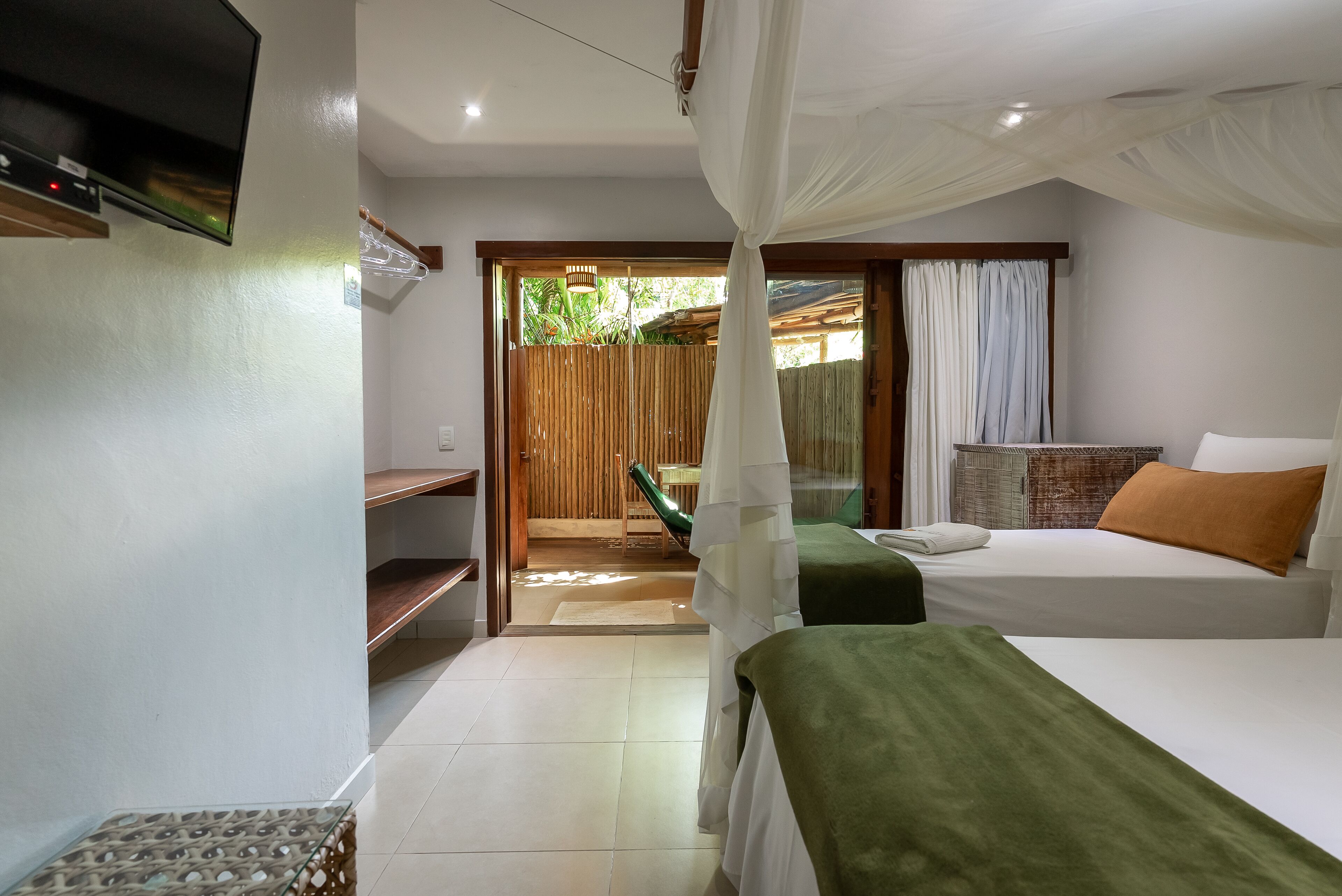 A bedroom with a bed, a green blanket, a white canopy, a wooden door, and a view of the outdoors.