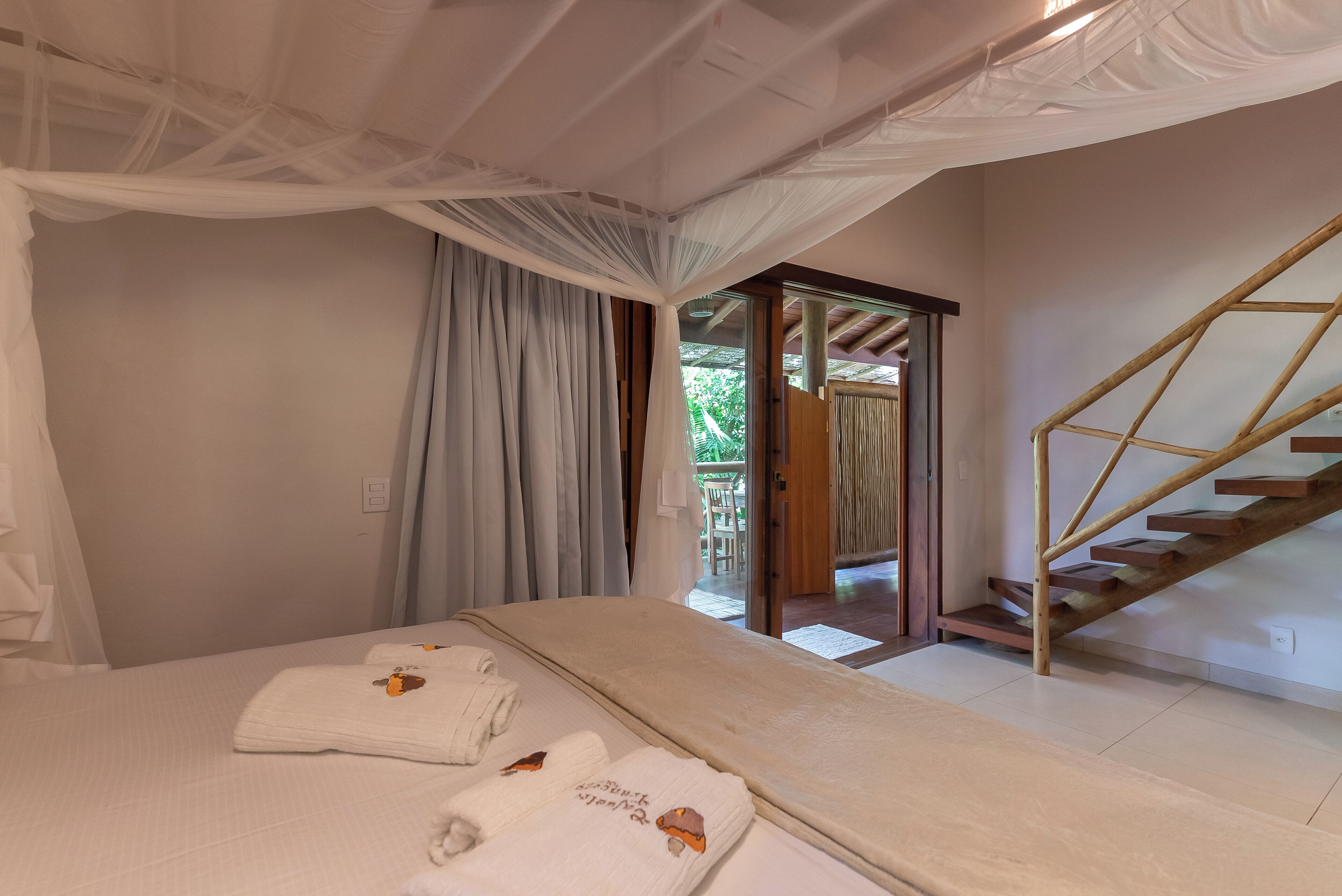 A bedroom with a bed, two towels, a canopy, a wooden staircase, and a door leading outside.