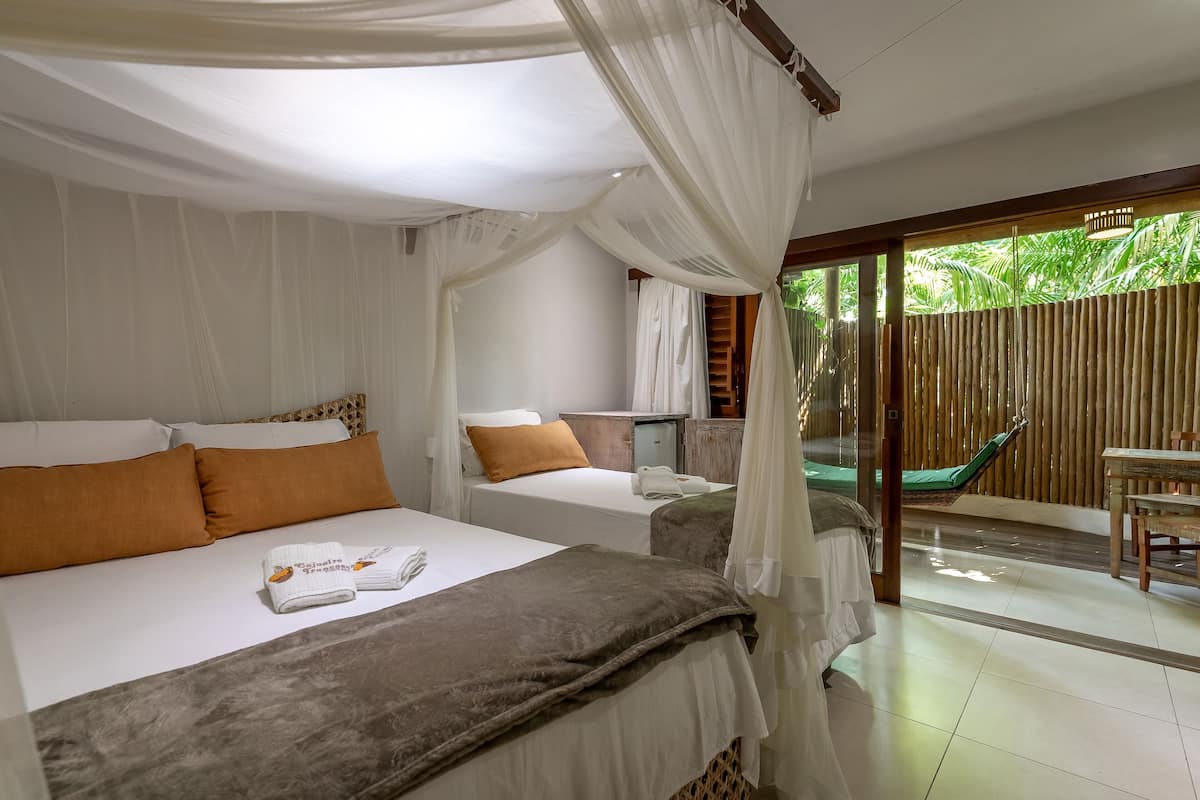 Ein Schlafzimmer mit zwei Betten, einem Himmelbett, einem kleinen Tisch, einem Stuhl und Blick ins Grüne.