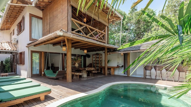 A wooden house with a pool, outdoor furniture, and a covered area with hanging lights.