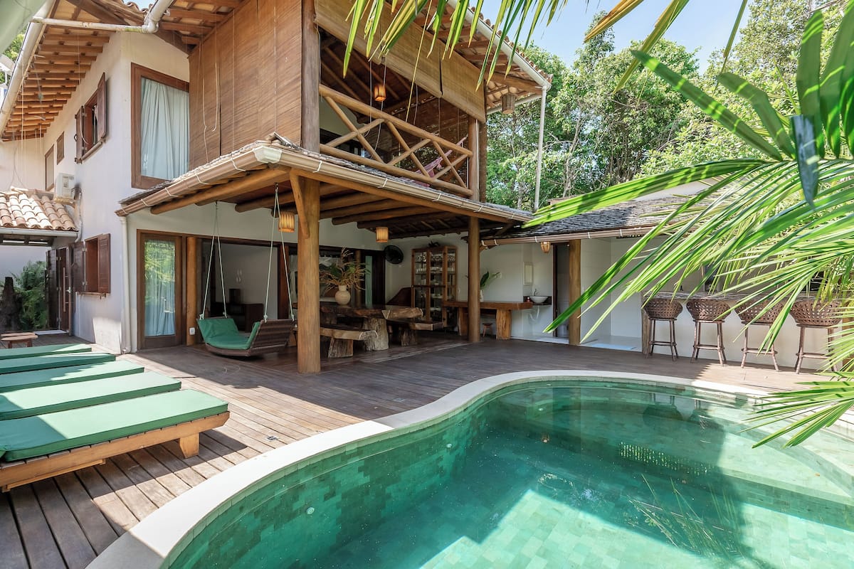 Ein Holzhaus mit Pool, Gartenmöbeln und einem überdachten Bereich mit hängenden Lichtern.