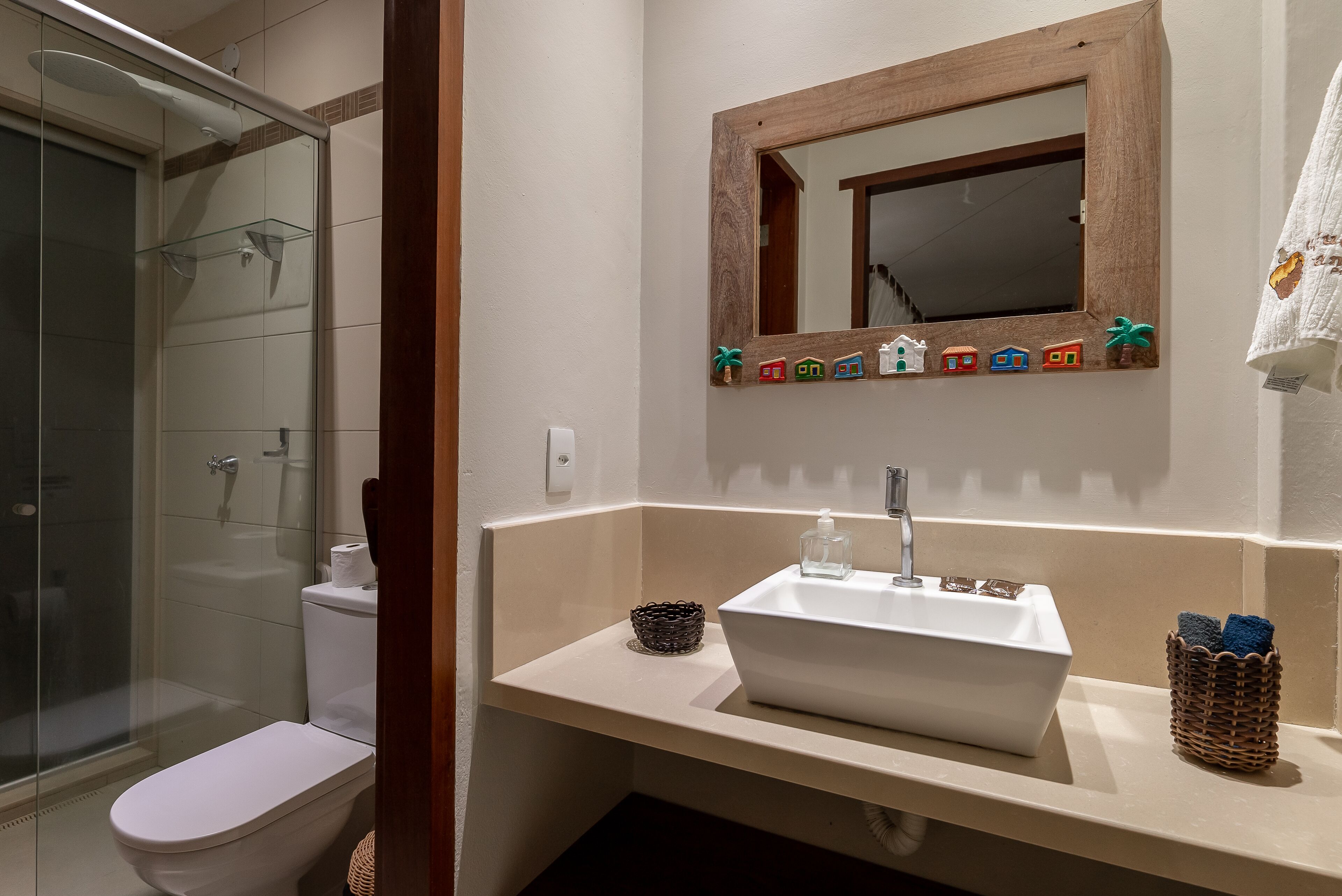 Un baño con cabina de ducha de vidrio, un inodoro, un lavabo con espejo y un perchero con toalla.