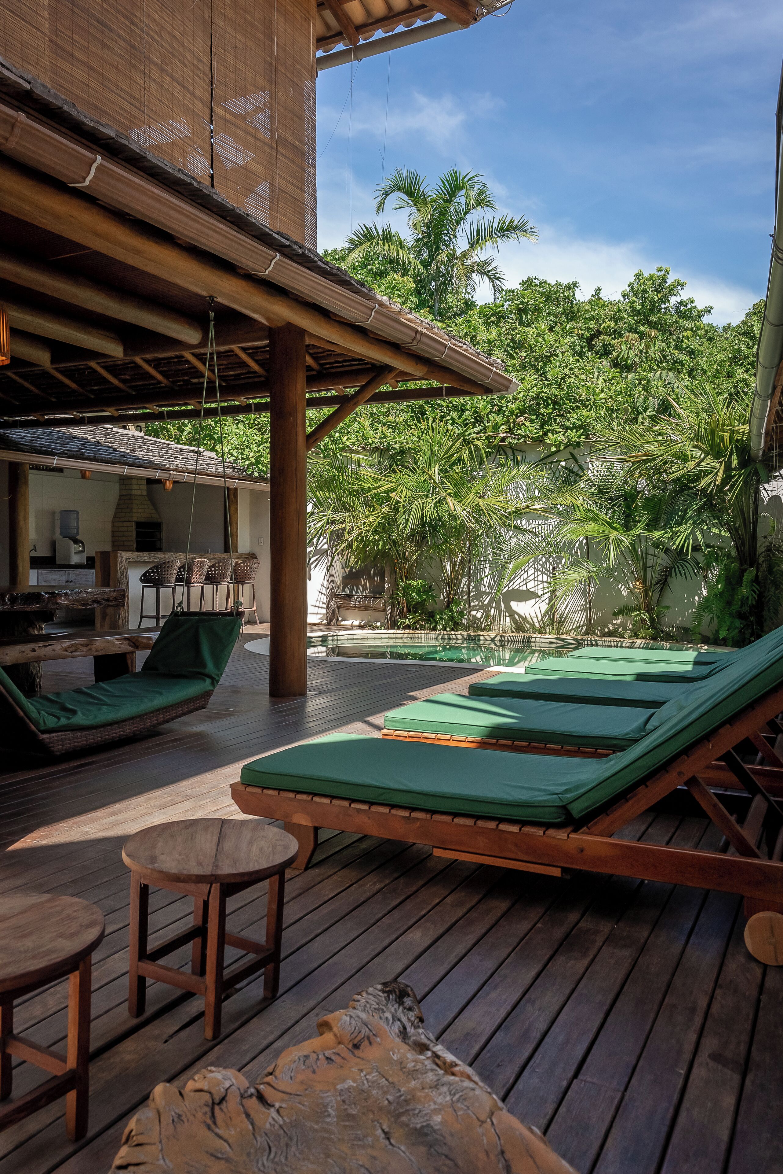 A wooden deck with lounge chairs and a table, surrounded by lush greenery and a clear sky.
