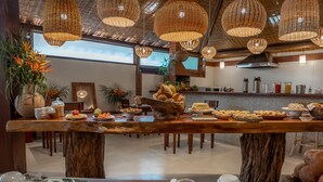A dining area with a long wooden table set for a meal, surrounded by wicker pendant lights, and a view of the kitchen in the background.