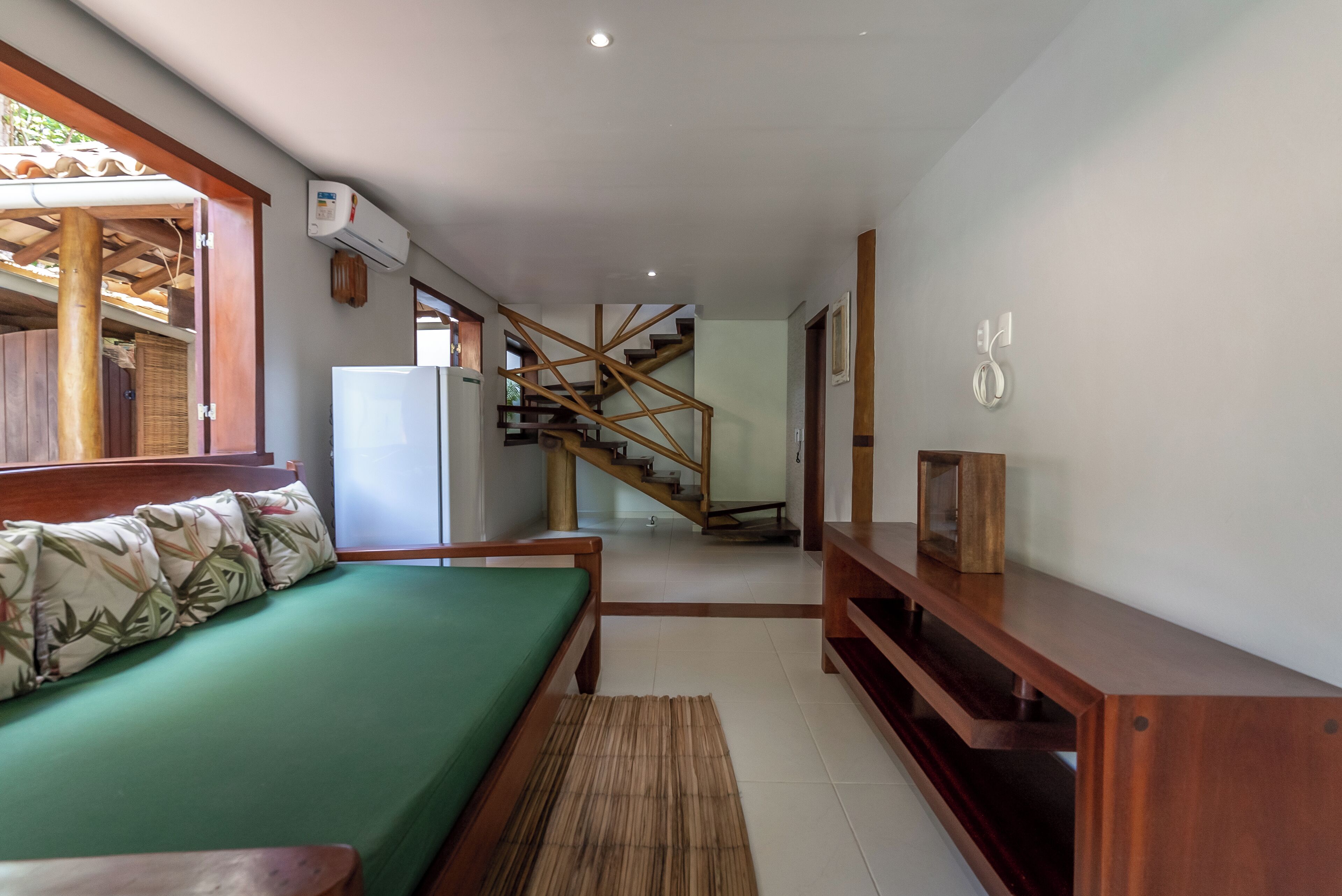 A room with a bed, a wooden bench, a staircase, and a wall-mounted air conditioner.