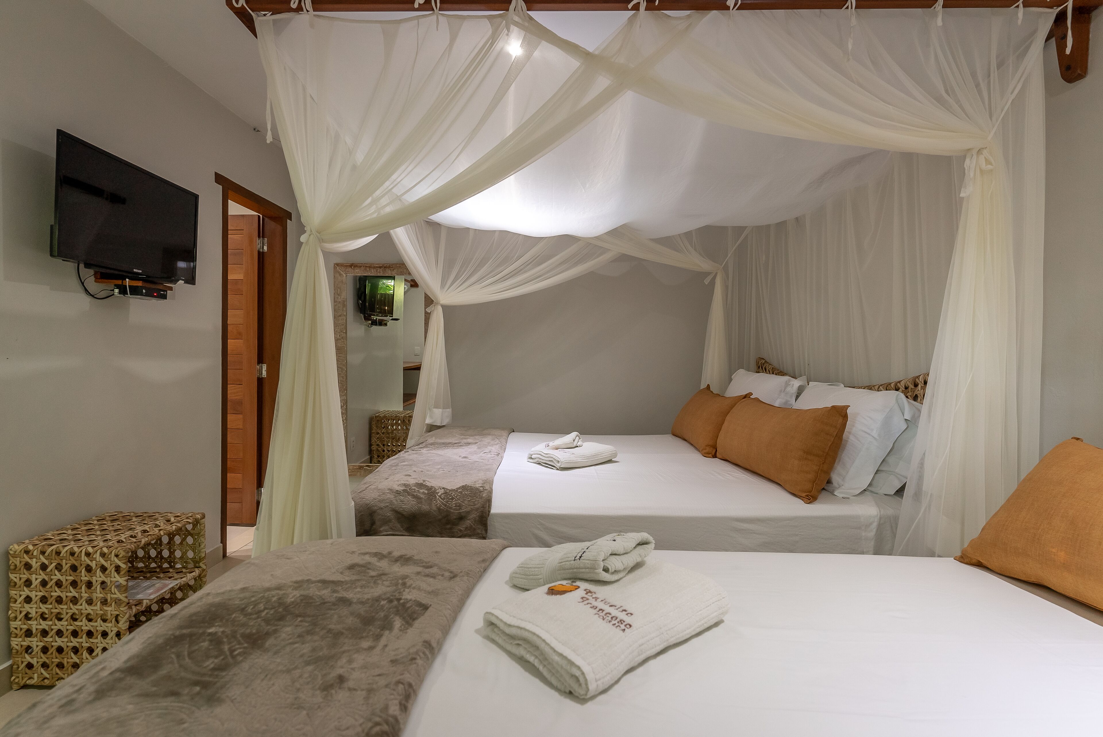 A room with two beds, a television, and a wicker side table.