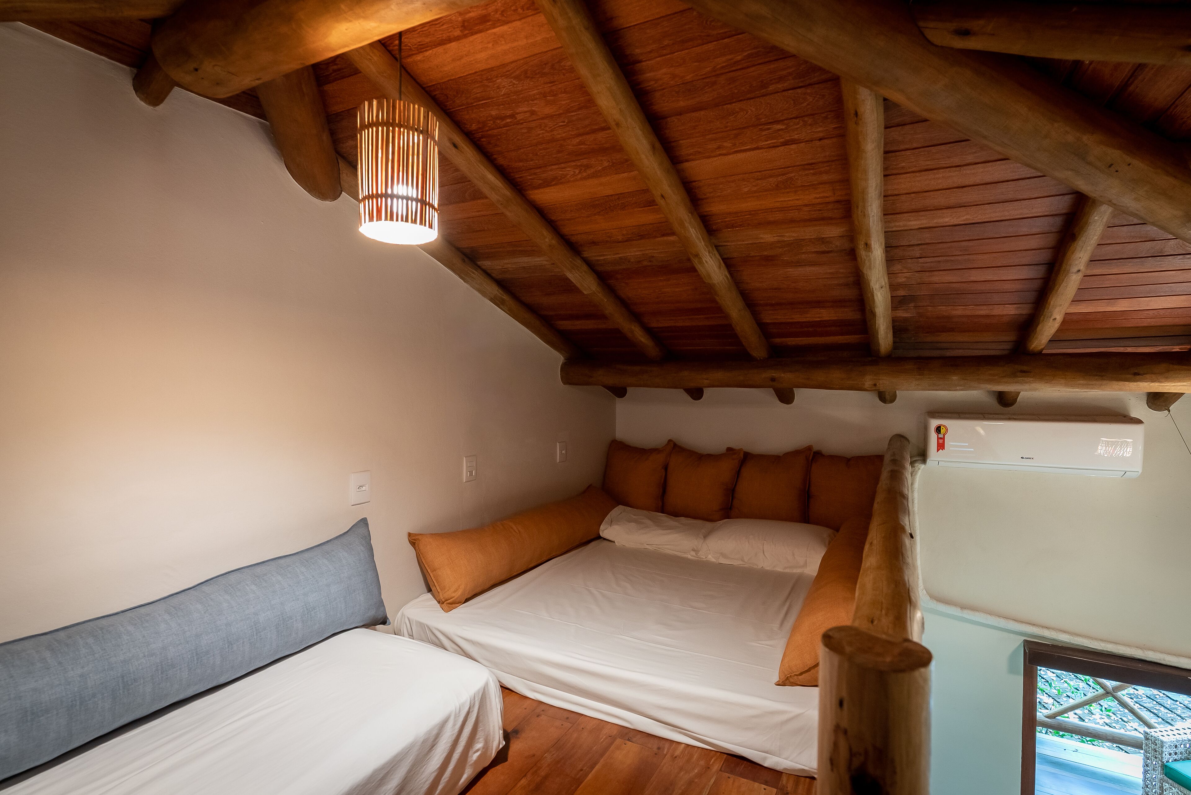 Una habitación acogedora con techo de madera, una cama con ropa blanca, una mesita y un aire acondicionado instalado en la pared.