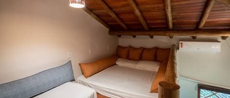 Una habitación acogedora con techo de madera, una cama con ropa blanca, una mesita y un aire acondicionado instalado en la pared.