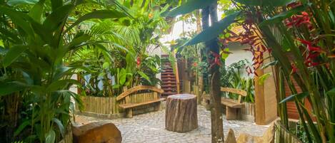 A paved pathway with wooden benches and a wooden archway surrounded by lush greenery and plants.
