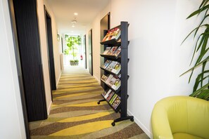 Un couloir avec un tapis à rayures, une bibliothèque et un fauteuil vert.