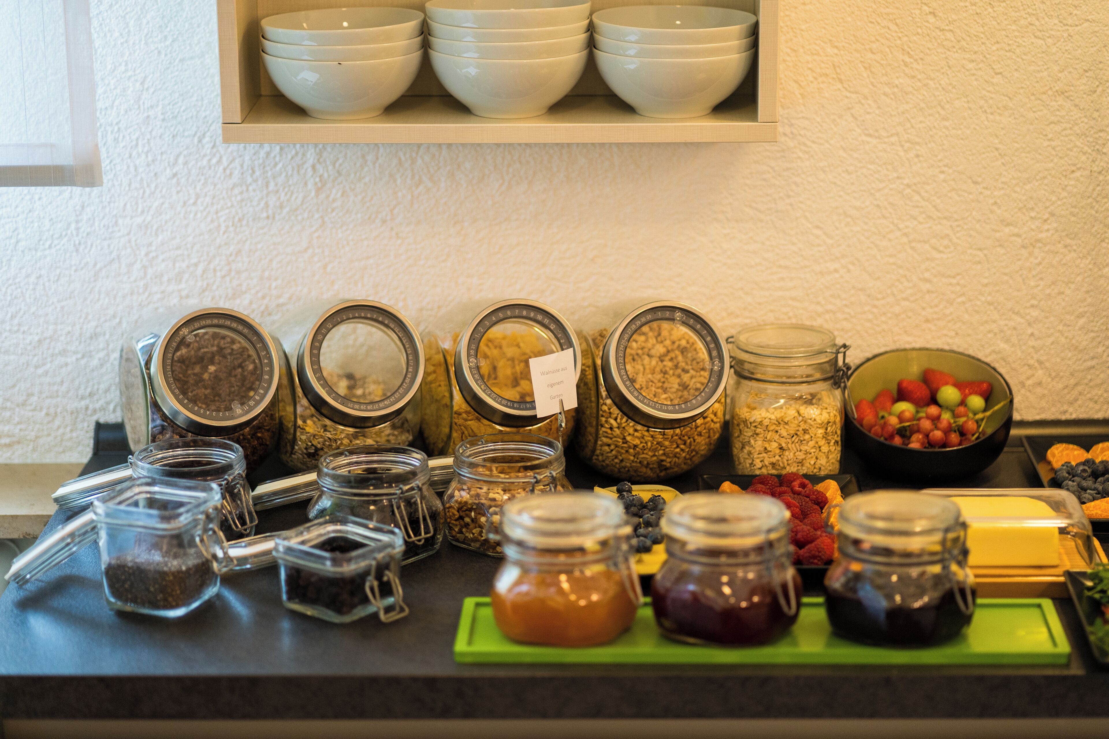 A variety of food items and containers on a counter, including jars of honey, jams, and nuts.