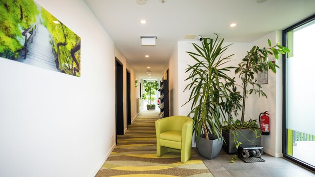 A hallway with a yellow chair, large potted plants, and a fire extinguisher on the wall. -  B&B Outlet Hotel – Metzingen – Bad Urach - Free Parking (Dettingen an der Erms)
