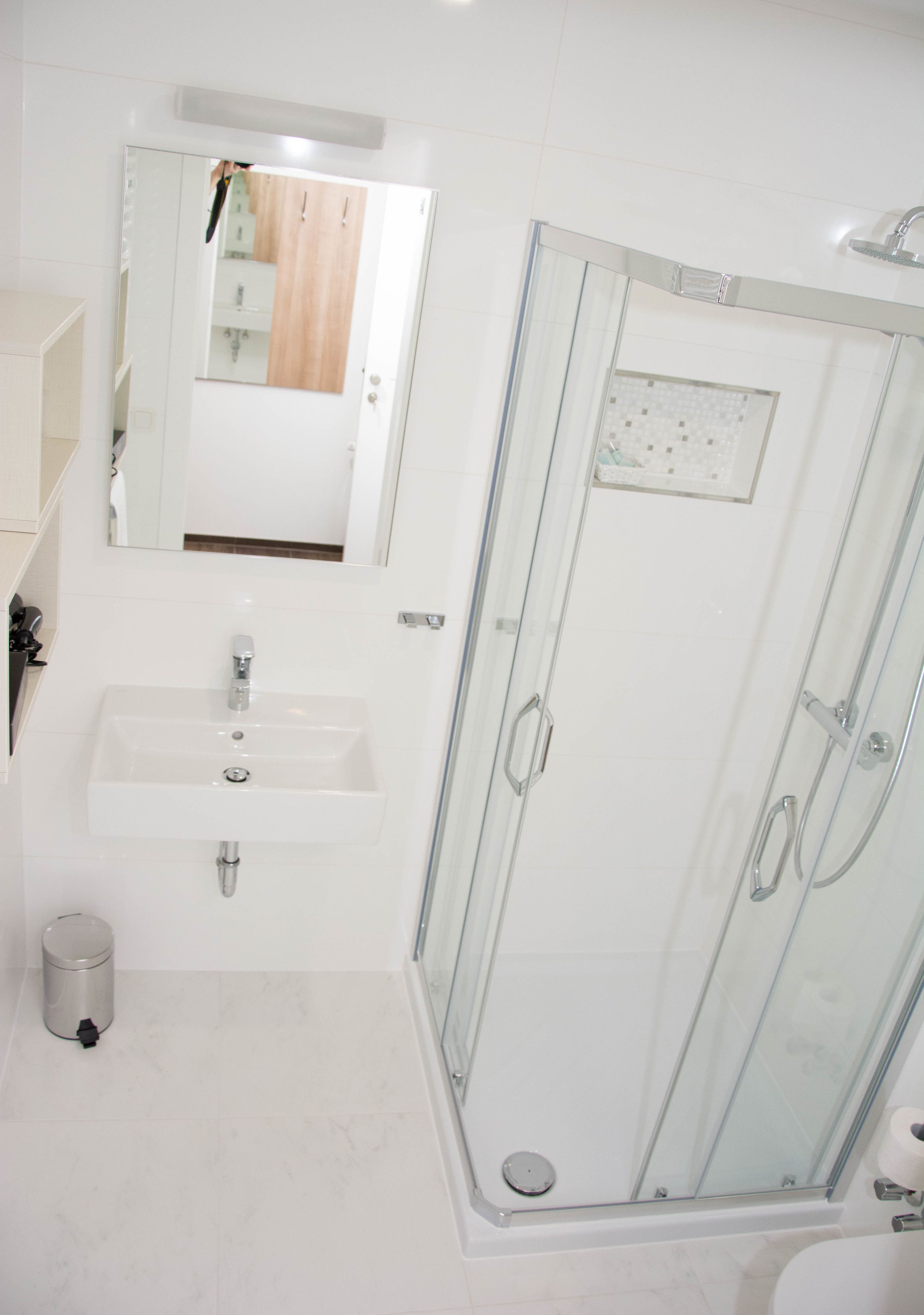 Un baño con ducha separada por mampara de vidrio, lavamanos y espejo.