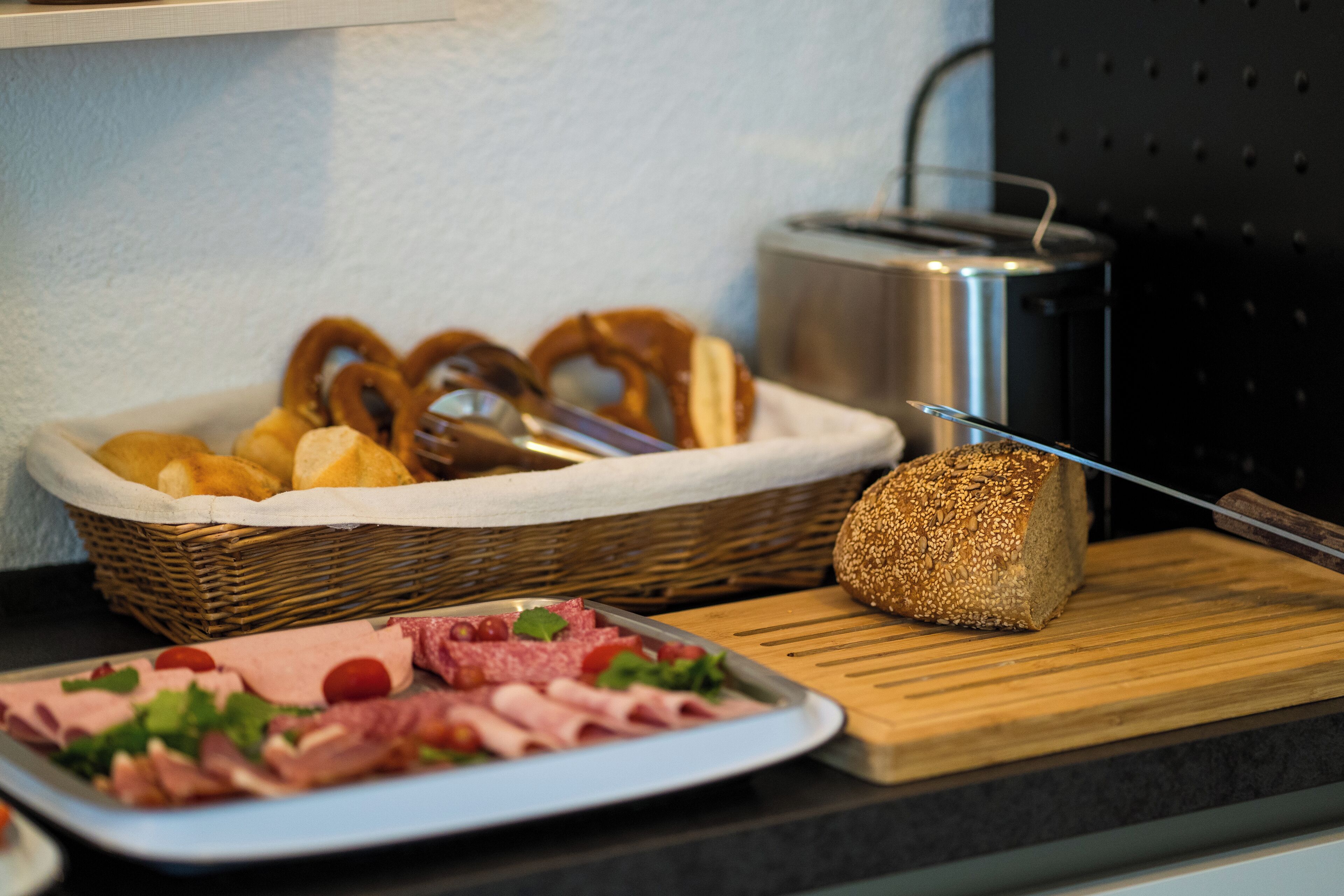 A breakfast buffet with sliced meats, bread, and pretzels.