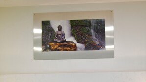 A hotel room with a wooden headboard, green and white pillows, a bed with green and white bedding, and a framed picture of a Buddha statue with a waterfall. -  B&B Outlet Hotel – Metzingen – Bad Urach - Free Parking (Dettingen an der Erms)
