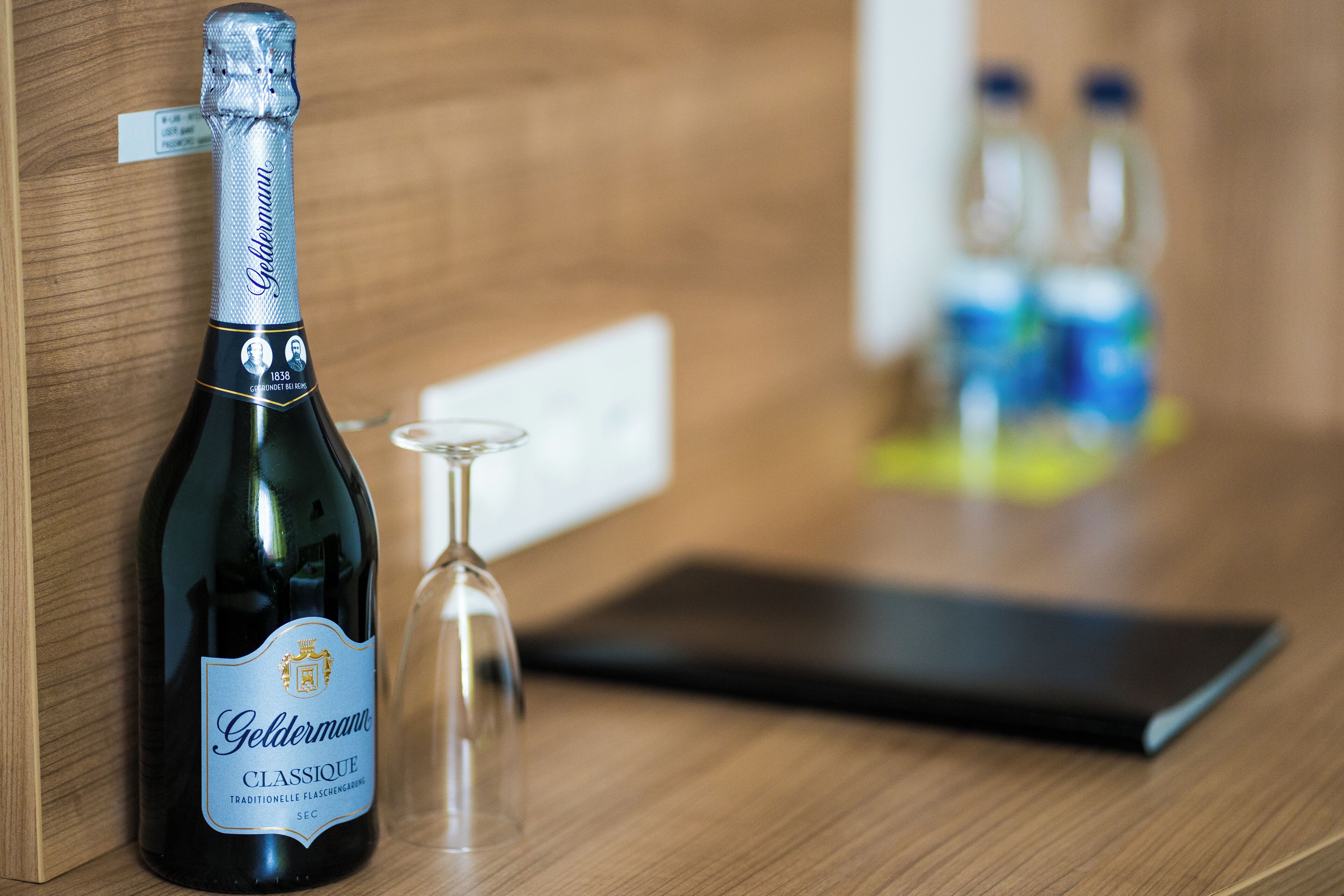 A bottle of Goldmann Classic wine, a wine glass, and a tablet on a wooden surface.