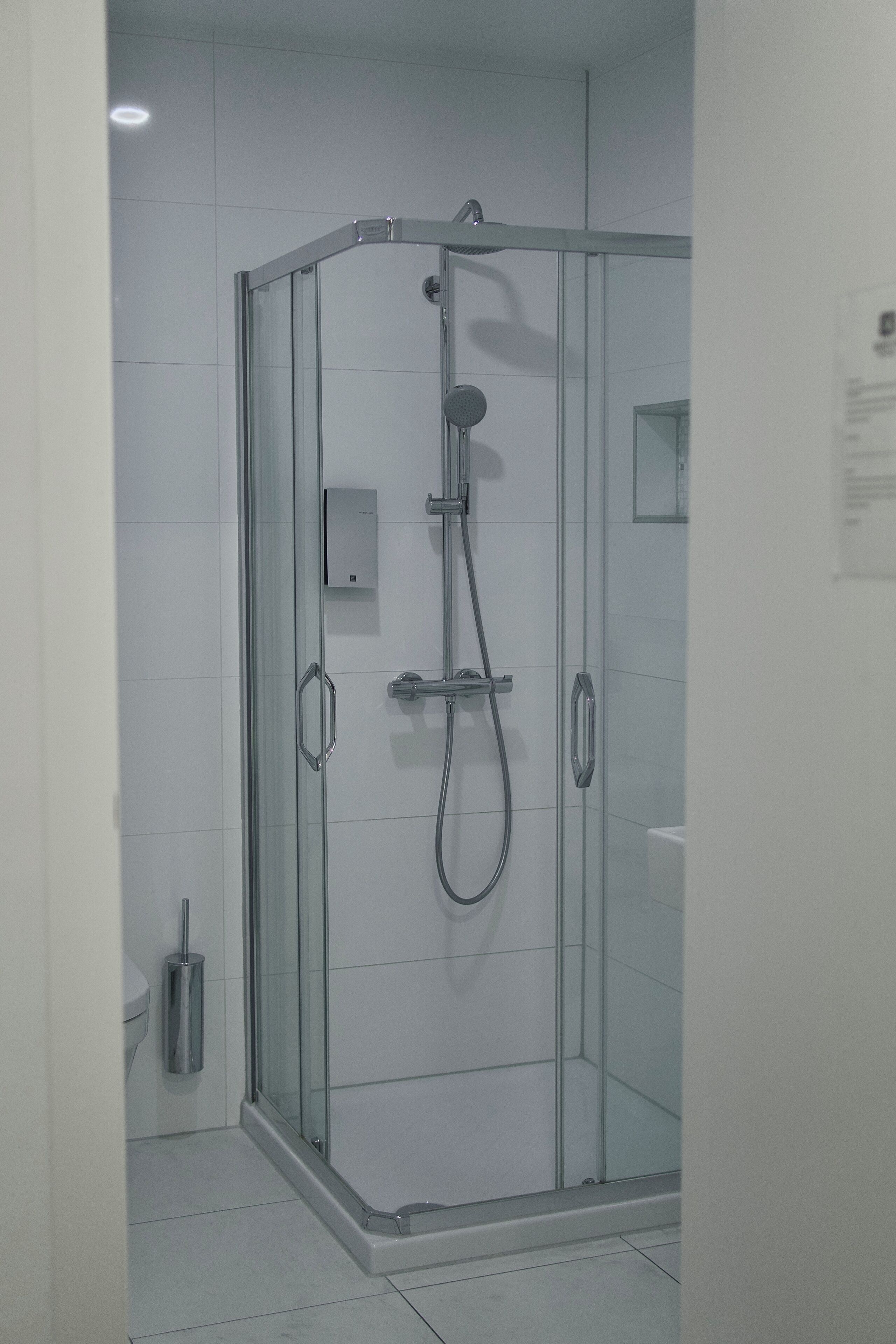 A modern shower enclosure with a glass door, a handheld showerhead, and a wall-mounted control panel.