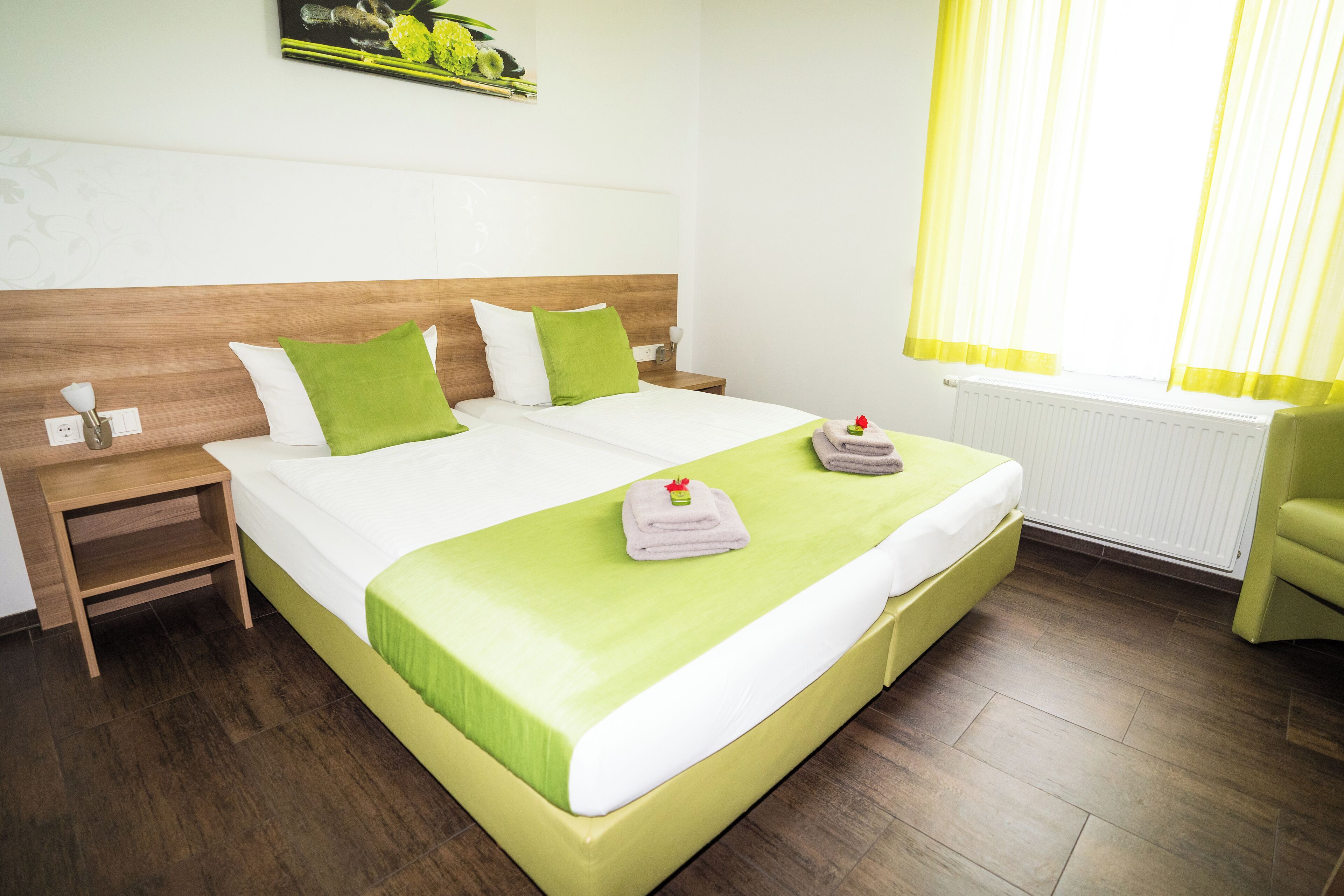 A neatly made bed with green and white bedding, a wooden headboard, and a nightstand with a lamp.
