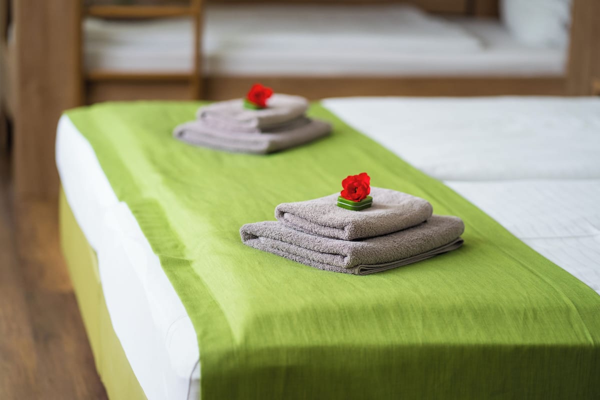 Un lit bien fait, recouvert d’une couverture verte, avec deux serviettes pliées posées sur le dessus, ornées de fleurs rouges.