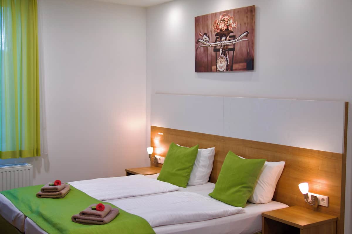 Une chambre d’hôtel avec un lit double, une literie verte et blanche, deux oreillers verts, une tête de lit en bois, des lampes de chevet et un tableau au mur.