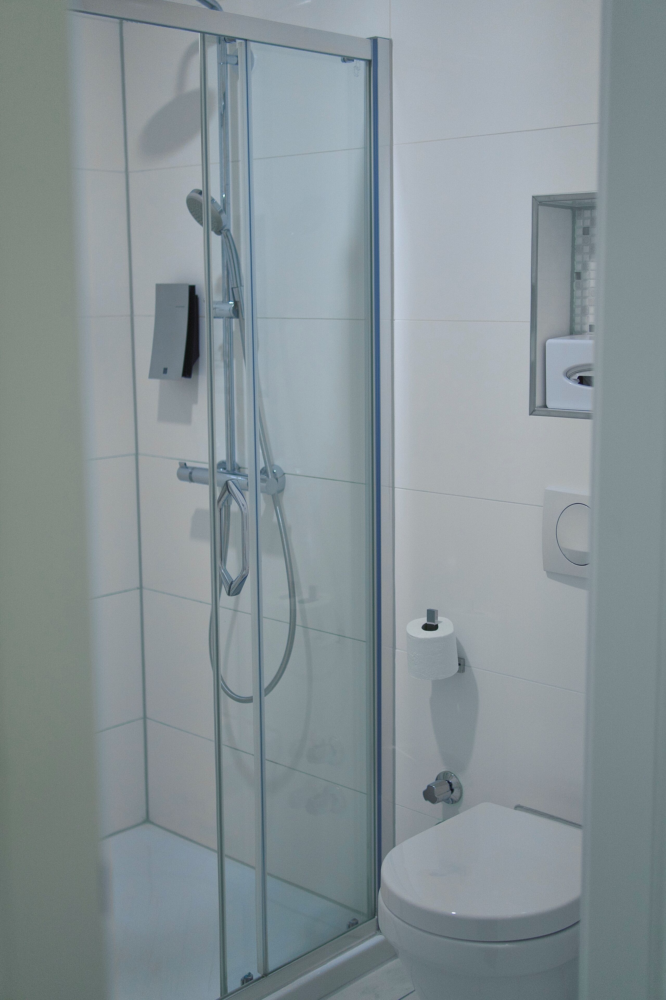 Un baño moderno con ducha de vidrio, inodoro y un espejo pequeño.