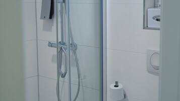 Un baño moderno con ducha de vidrio, inodoro y un espejo pequeño.