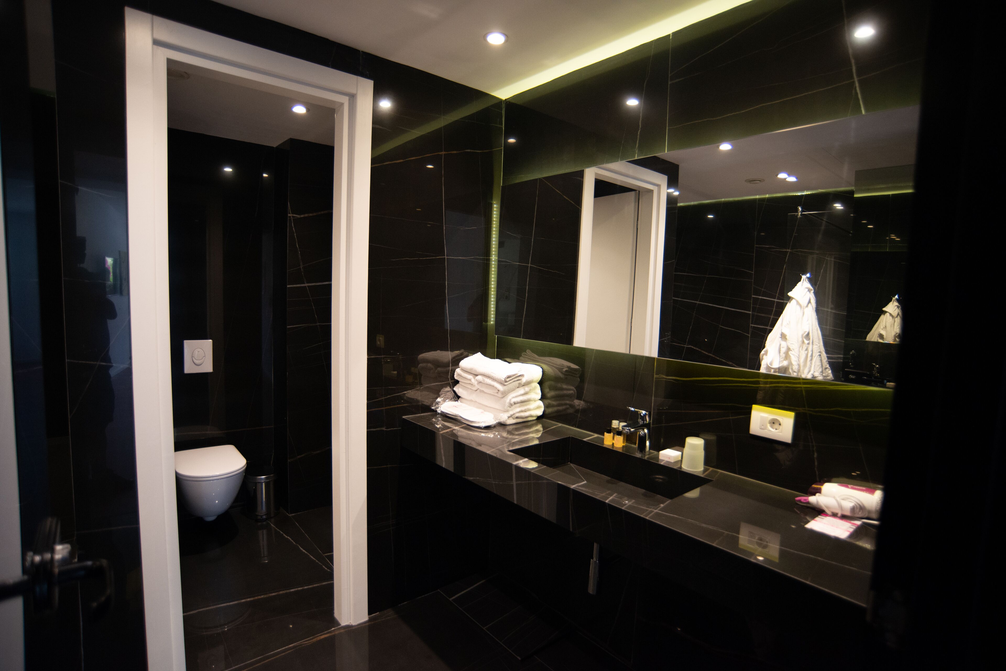 A modern bathroom with a dark marble vanity, a large mirror, and a white toilet.