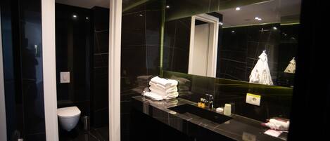 A modern bathroom with a dark marble vanity, a large mirror, and a white toilet.