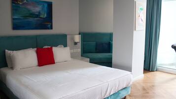 A modern hotel room with a large bed, a teal sofa, and artwork on the walls.