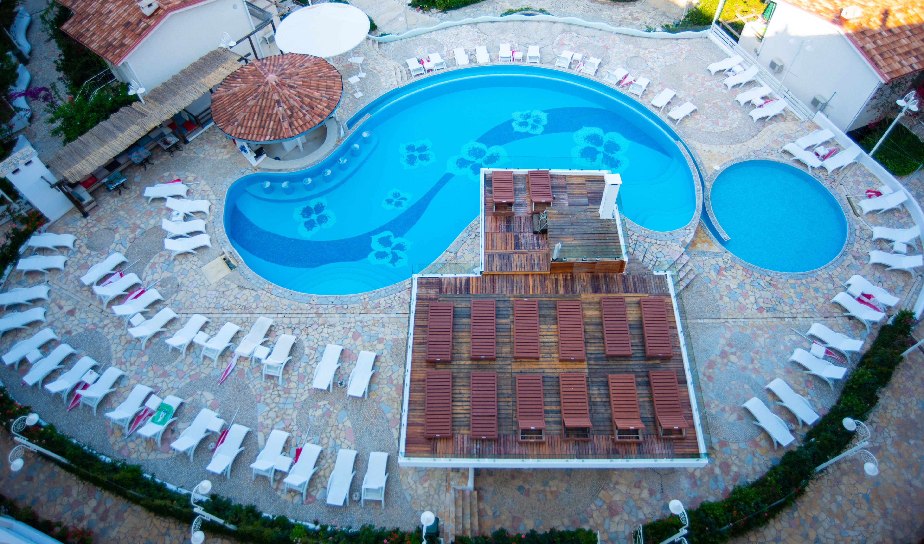 An aerial view of a resort with a large central pool, smaller pools, and numerous sun loungers arranged around the pools.