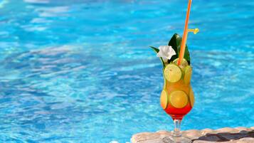 Ein Cocktail mit Limettenscheiben und einem Strohhalm in einem Glas, auf einer Steinfläche am Pool platziert.